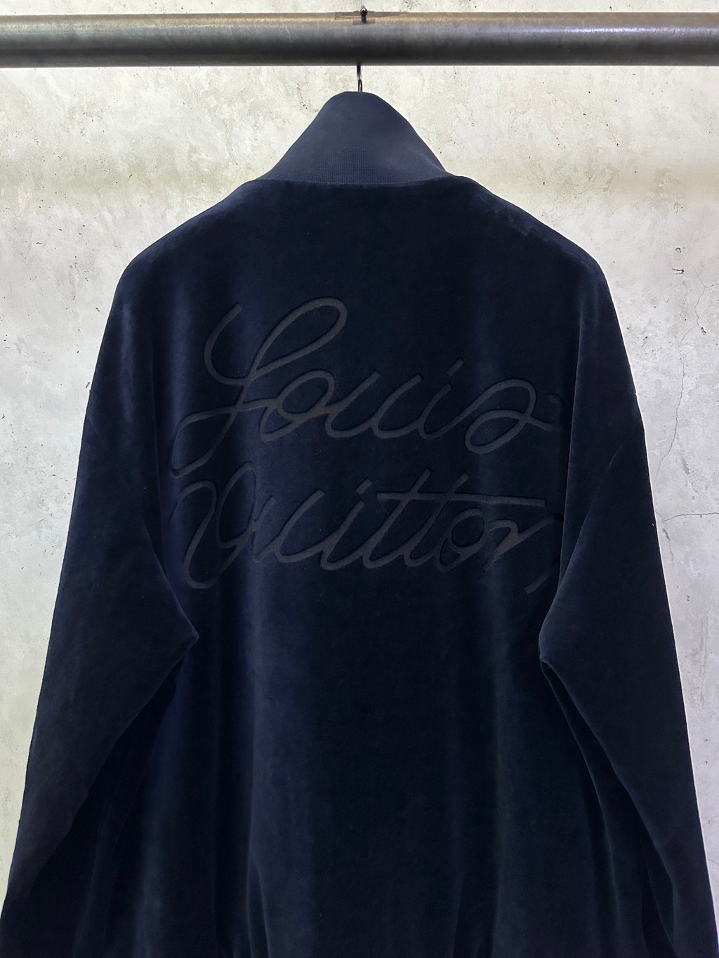 Dark navy zip-up jacket back view with subtle embossed cursive logo