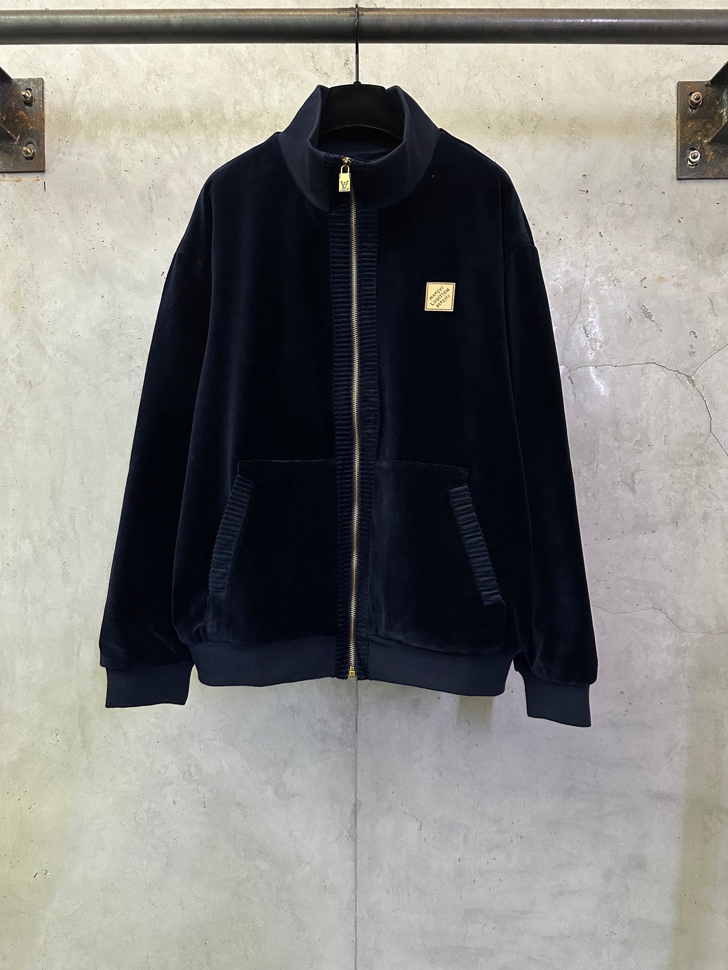 Dark navy zip-up jacket with stand collar, gold zipper pull, and small logo patch