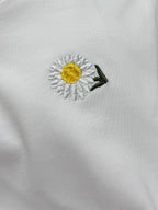 Daisy embroidery on white T-shirt, with yellow center and green leaves
