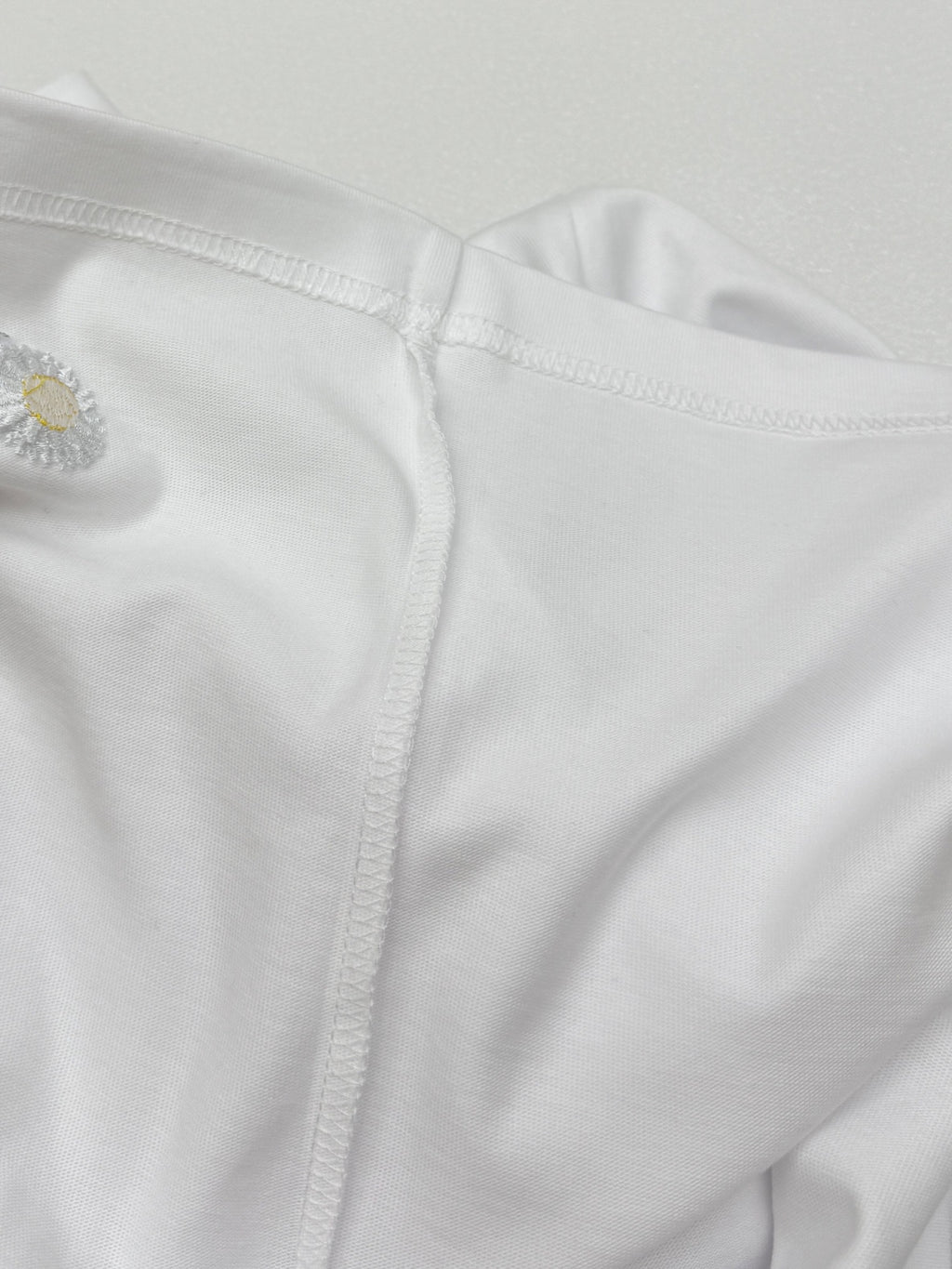 Side seam and embroidered daisy near hem on white T-shirt