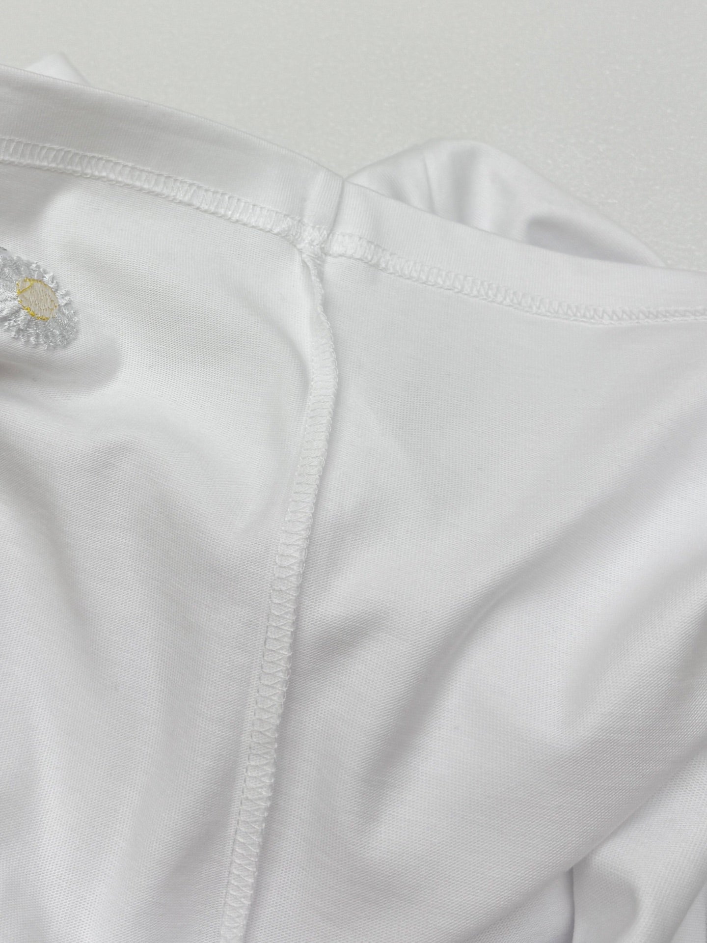 Side seam and embroidered daisy near hem on white T-shirt