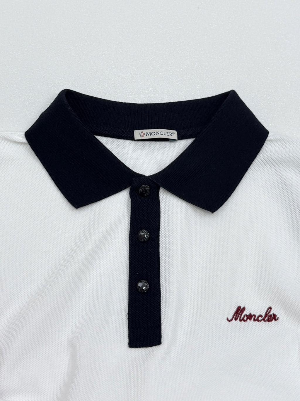 Moncler polo collar with black knit edge and three dark buttons, white shirt