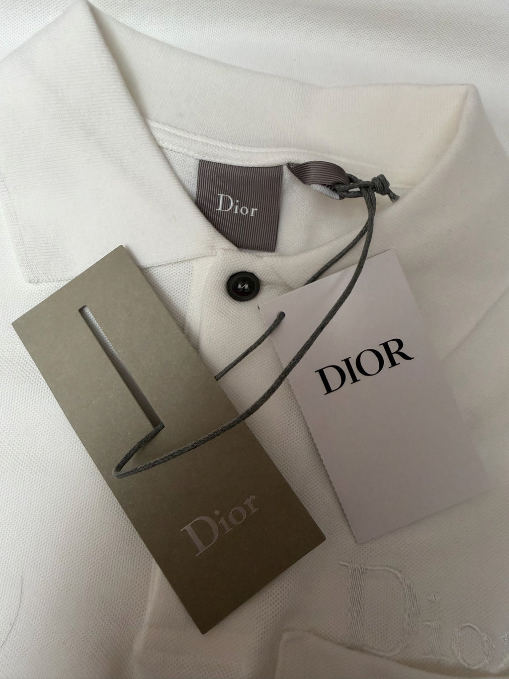 White Dior polo shirt with neck tag, Dior label, and product tags on fabric