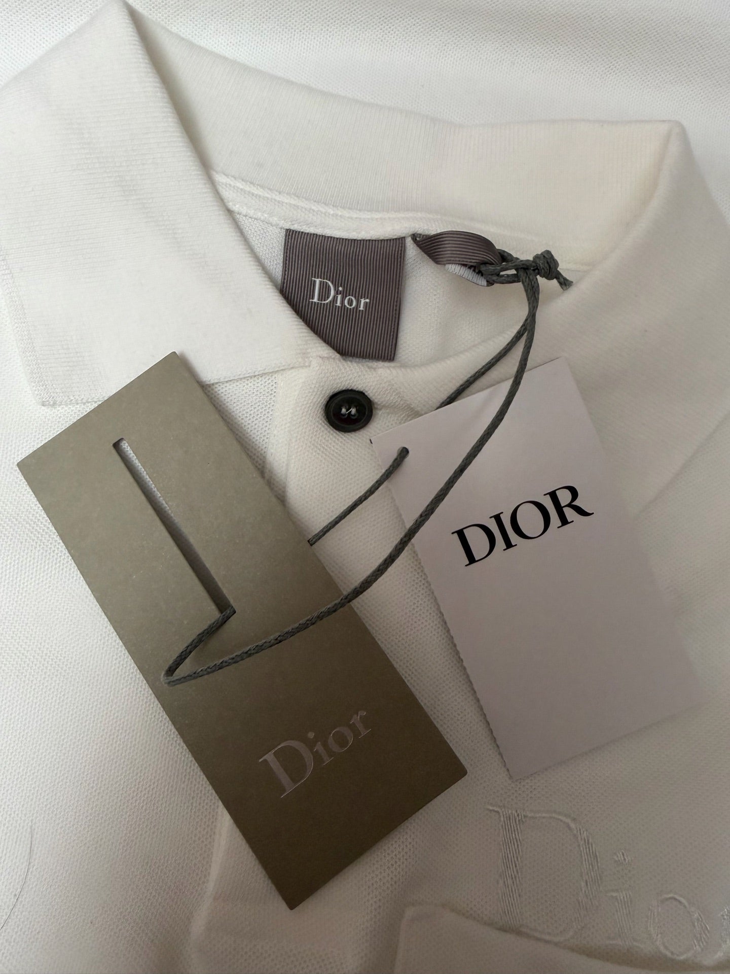 White Dior polo shirt with neck tag, Dior label, and product tags on fabric