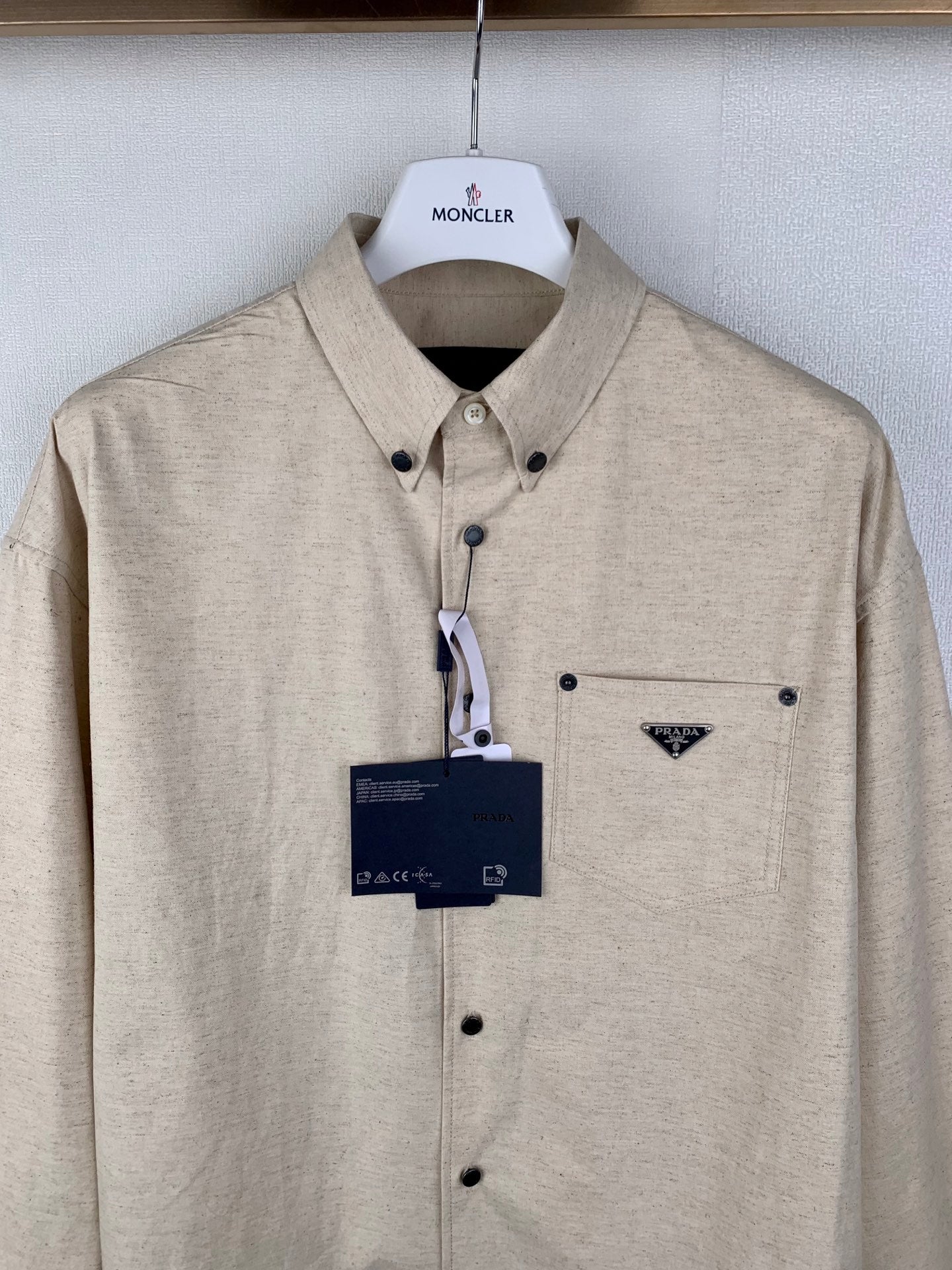 Beige long-sleeve button-up shirt with point collar, chest pocket, hanging tag