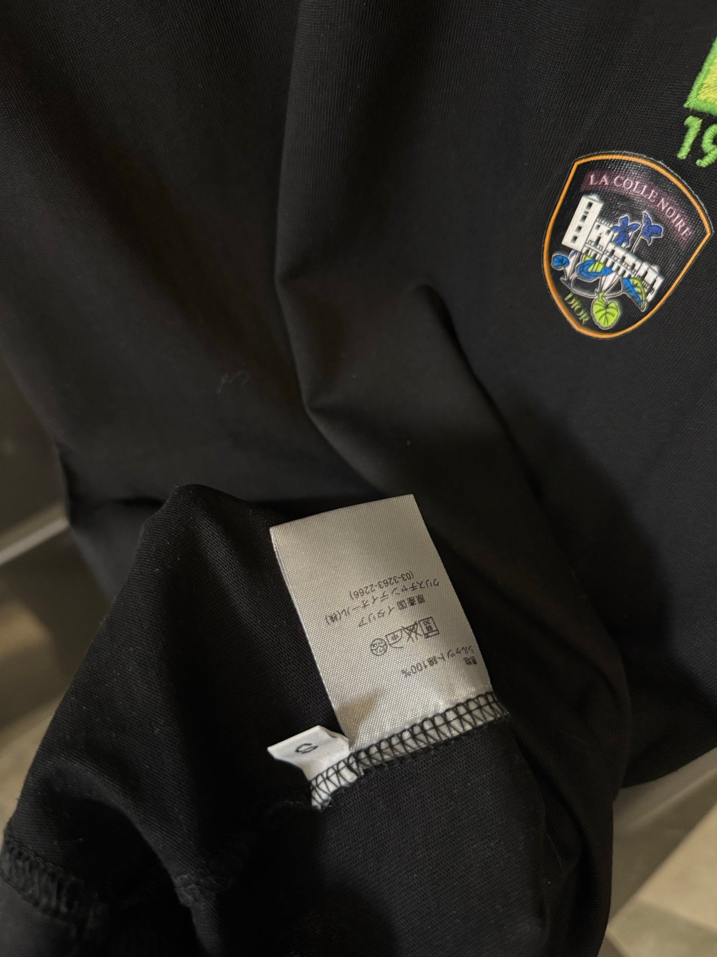 Black T-shirt sleeve with care label and small embroidered crest
