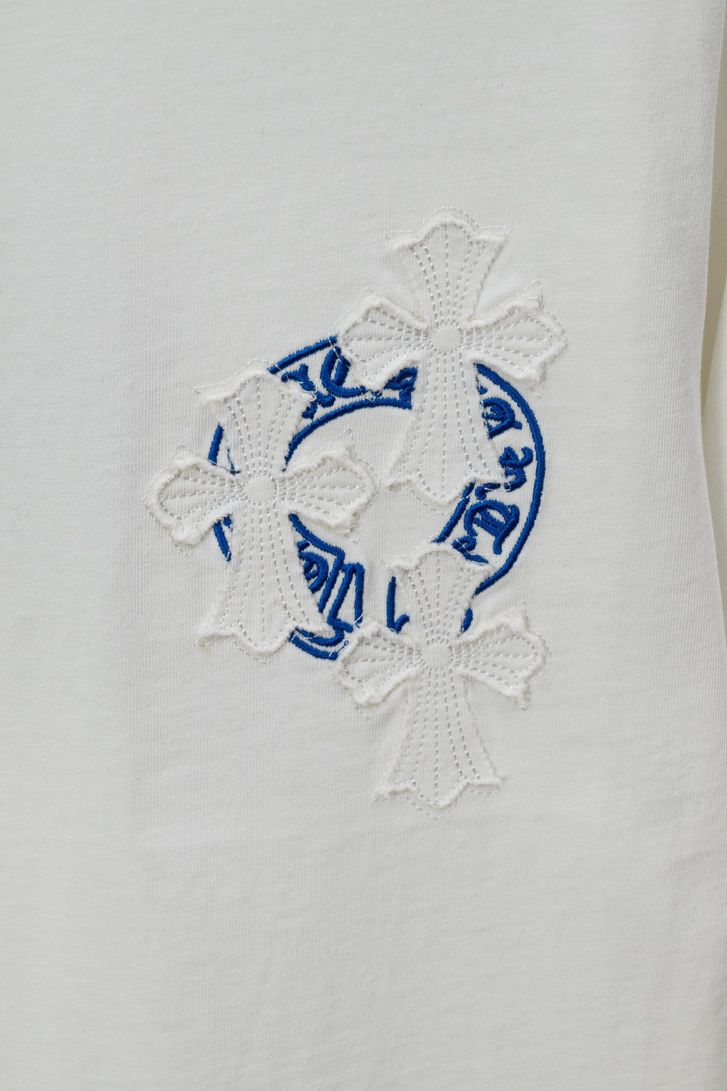 White T-shirt close-up of blue circular crest embroidery with cross-like textured details