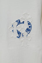 White T-shirt close-up of blue circular crest embroidery with cross-like textured details