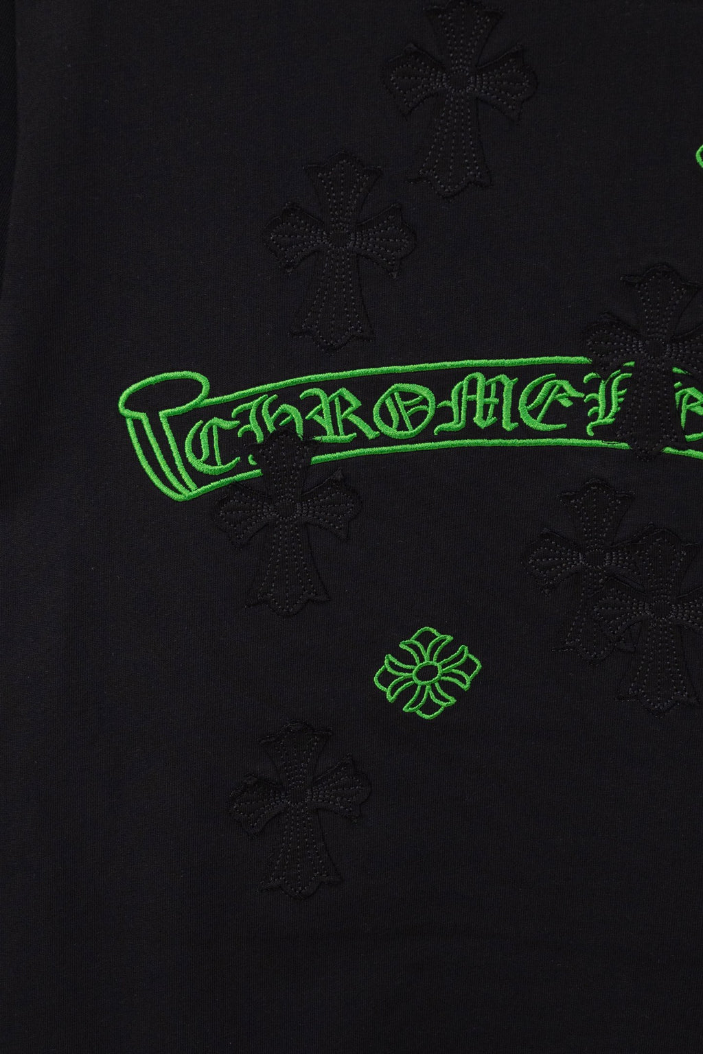 Black T-shirt close-up of green logo print with raised cross-like textured motifs