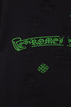 Black T-shirt close-up of green logo print with raised cross-like textured motifs