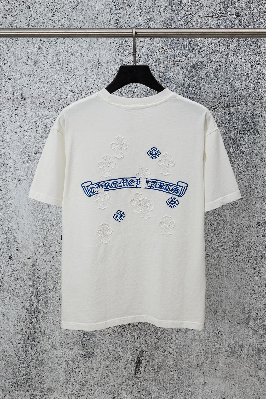 White graphic T-shirt with blue embroidered-style logo and small cross-like accents