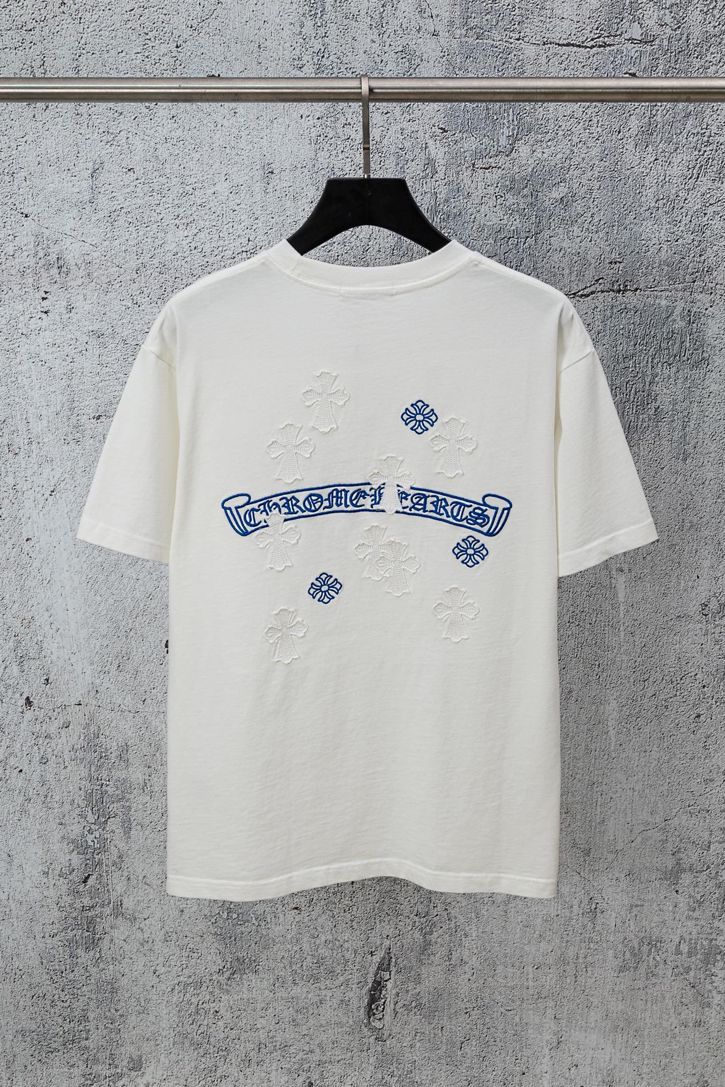 White graphic T-shirt with blue embroidered-style logo and small cross-like accents