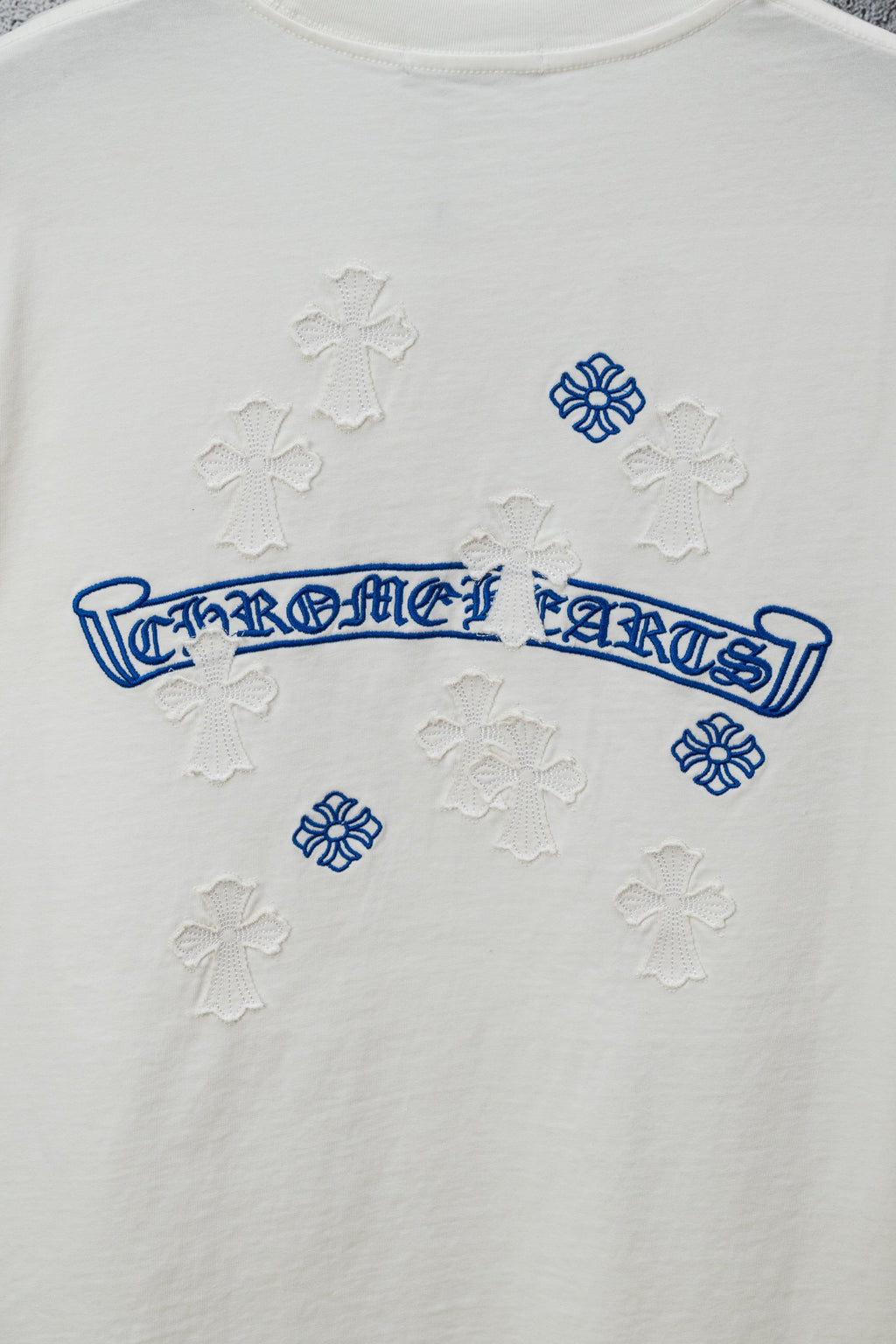 White T-shirt close-up of blue logo print and small raised cross-like patterns