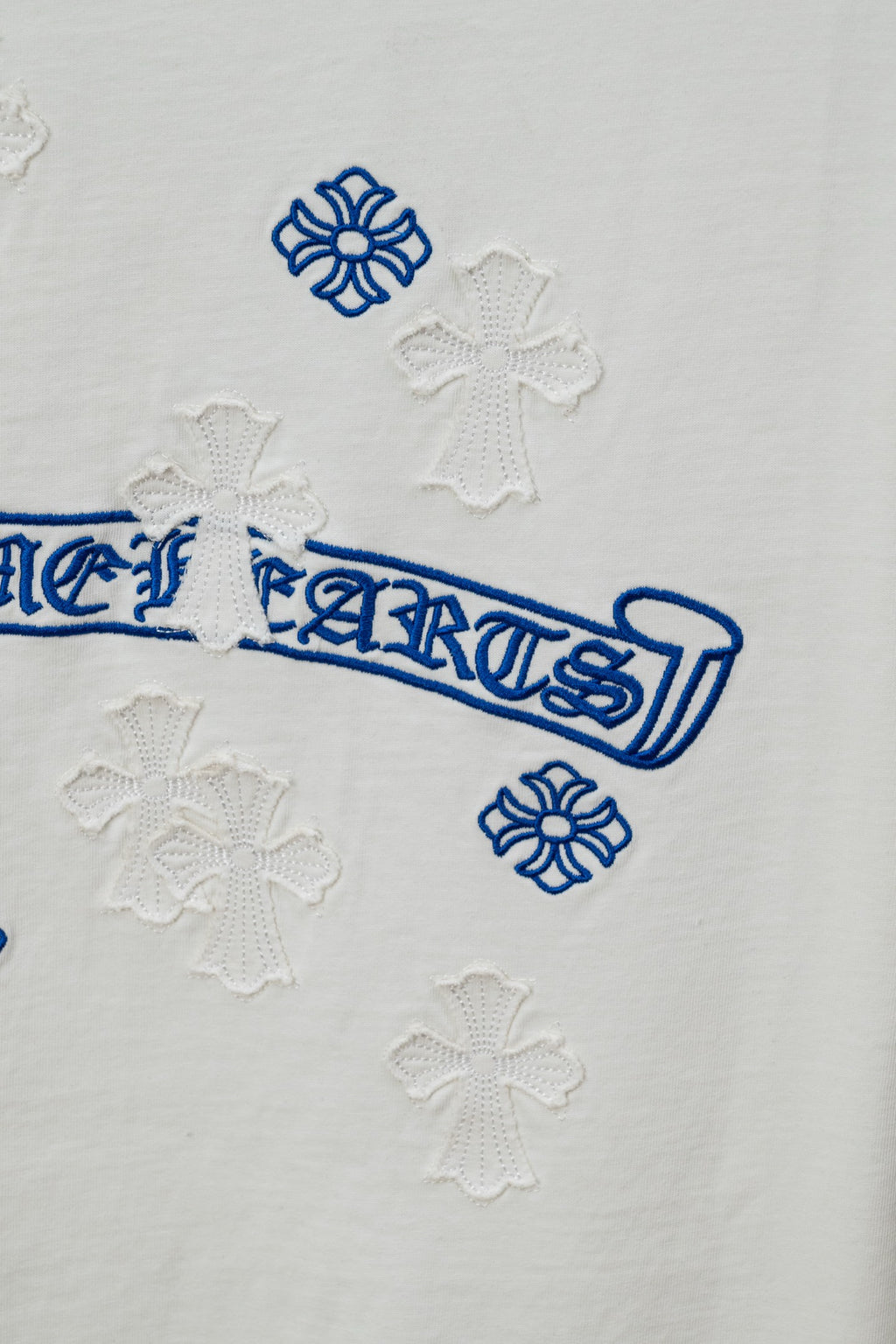 White T-shirt close-up of blue logo print and small cross-like raised embroidery