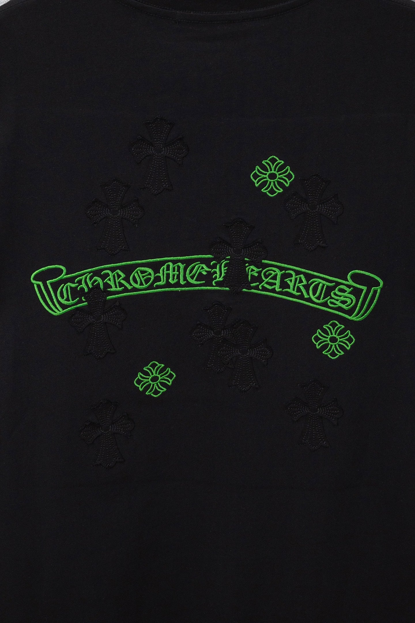 Black T-shirt close-up of green logo outline and small cross-like embroidery pattern