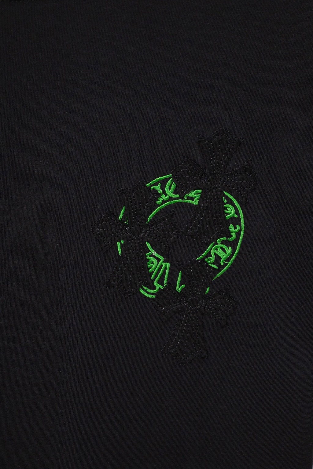 Black T-shirt close-up showing green crest-style patch with textured cross motif