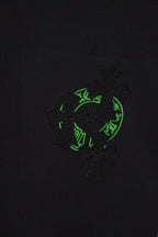 Black T-shirt close-up showing green crest-style patch with textured cross motif