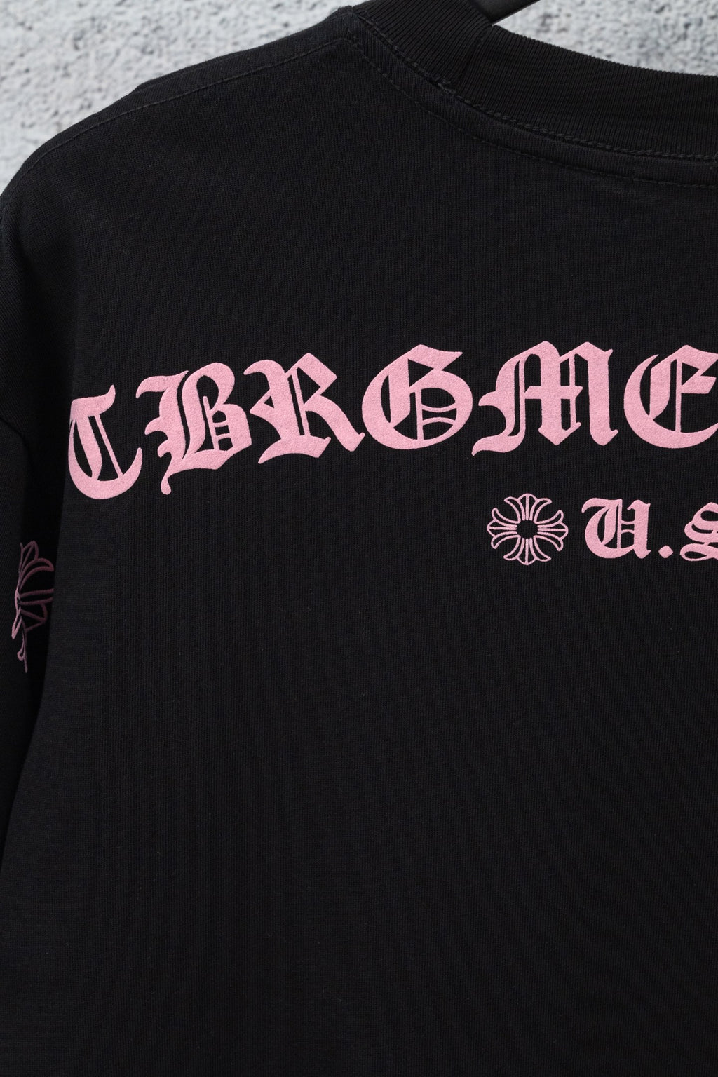 Black short-sleeve T-shirt with pink graphic lettering and small cross-flower emblem