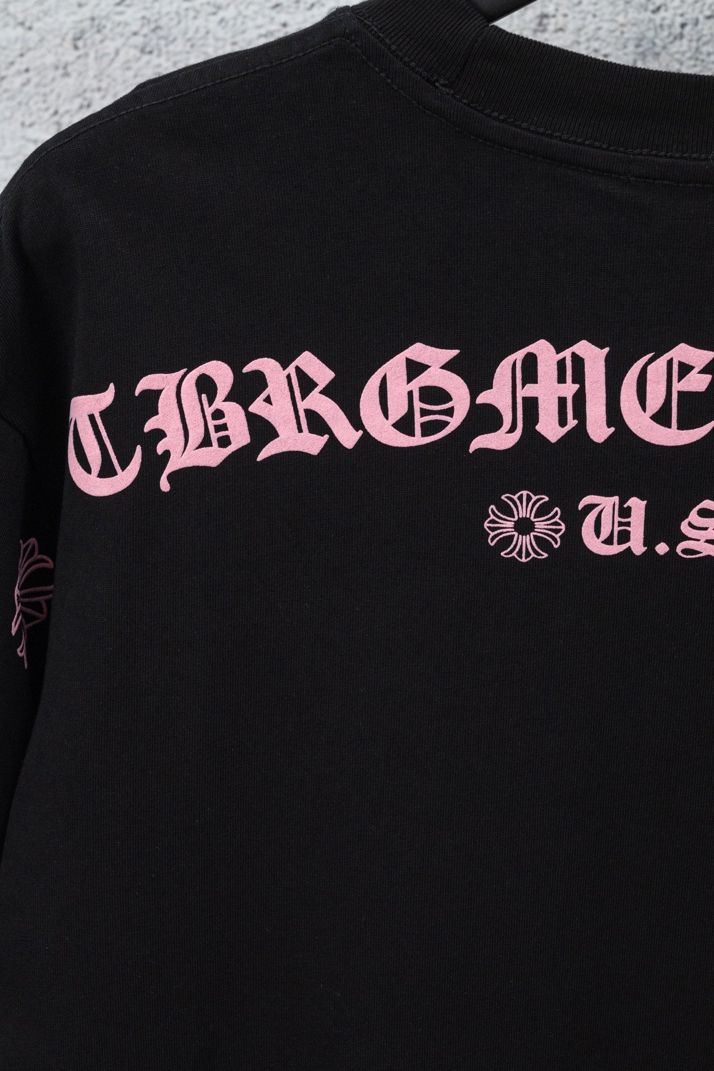 Black short-sleeve T-shirt with pink graphic lettering and small cross-flower emblem