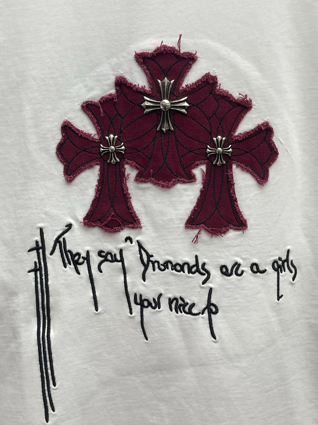White T-shirt chest graphic of maroon cross-like flowers with black handwritten script