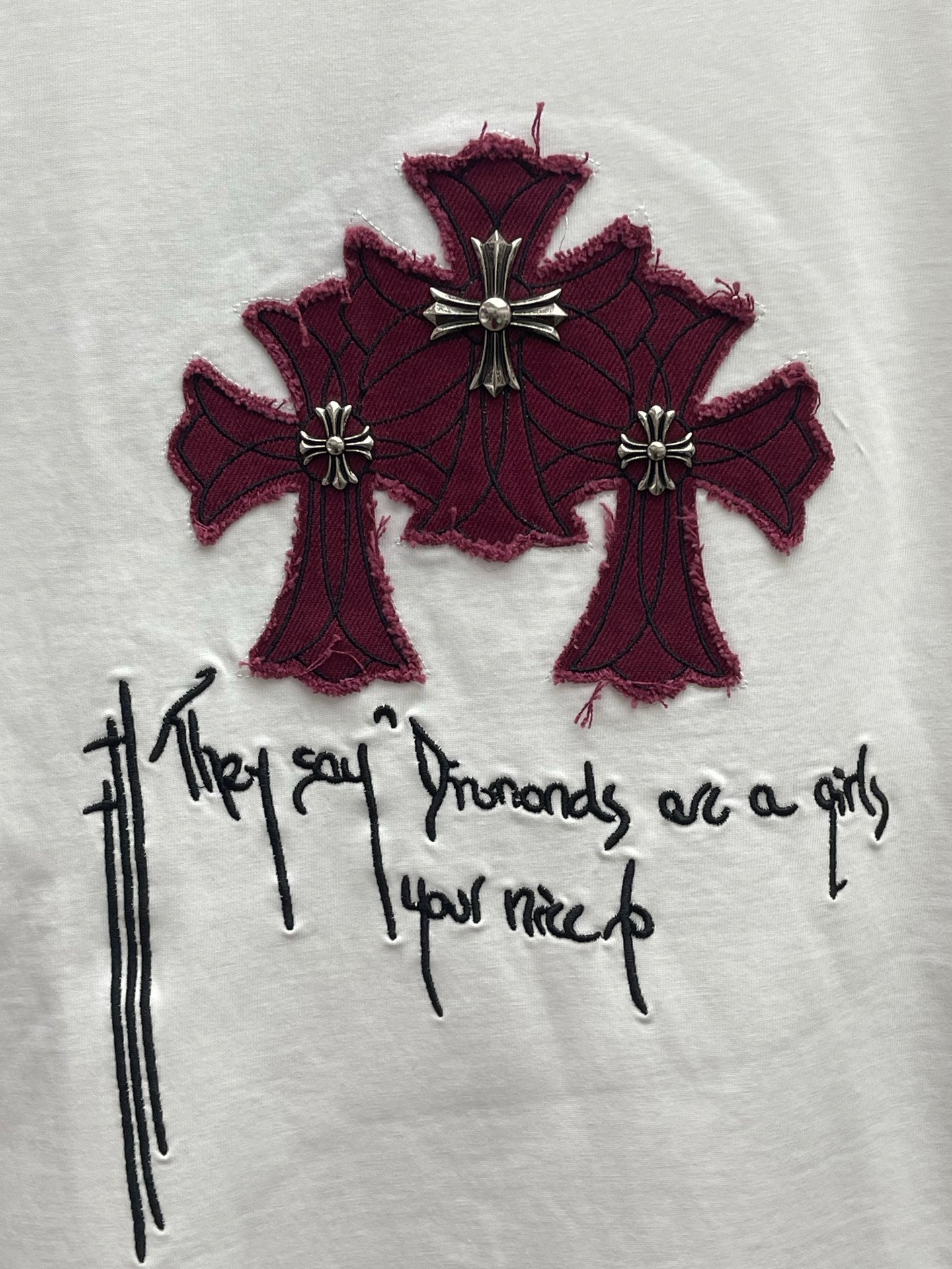 White T-shirt chest graphic of maroon cross-like flowers with black handwritten script