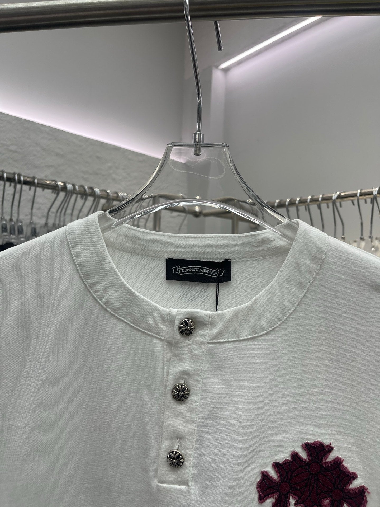 White short-sleeve T-shirt neckline with three dark buttons and maroon chest graphic