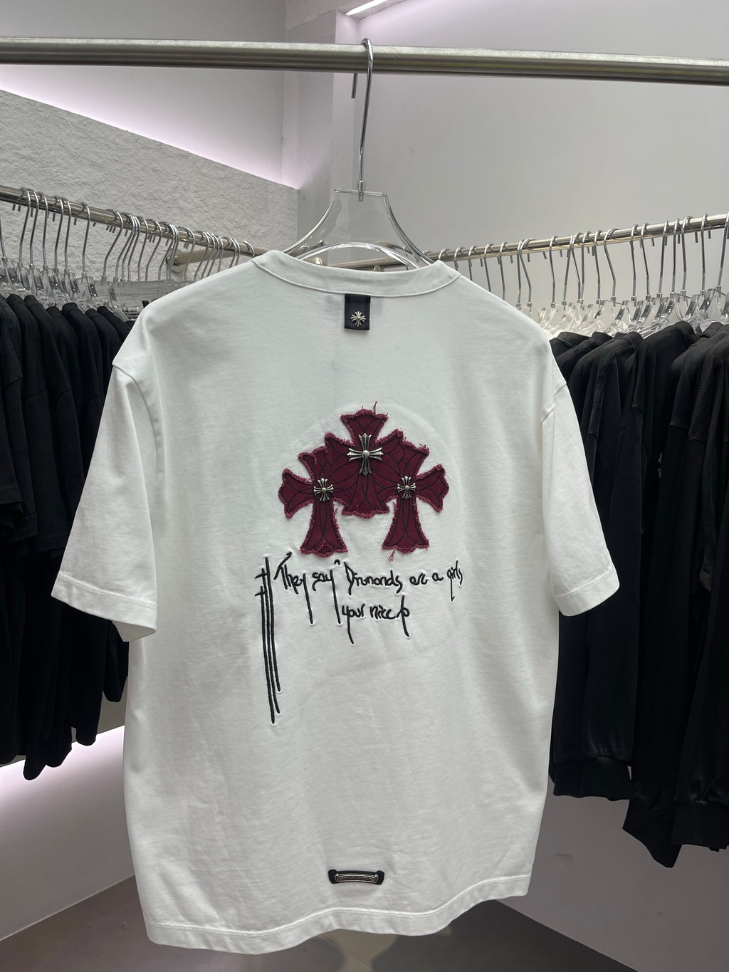 White short-sleeve T-shirt with centered maroon flower graphic and black script text