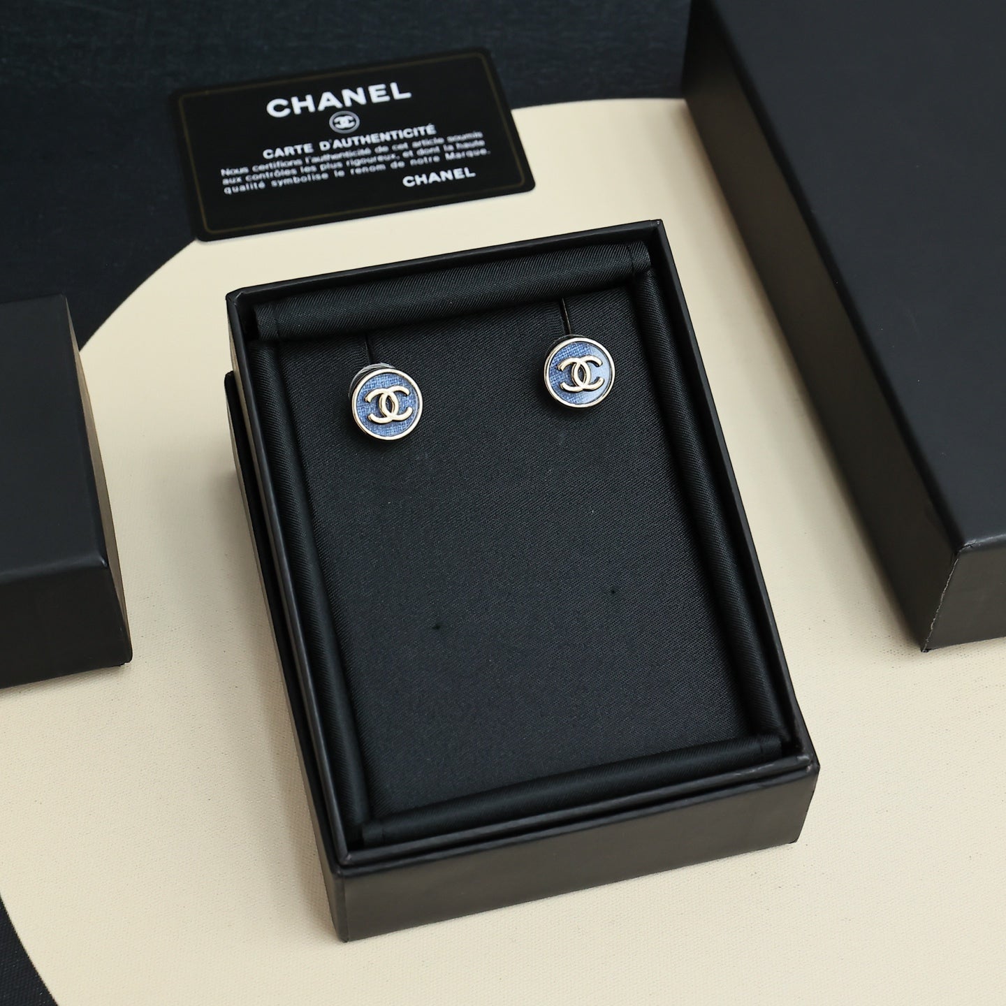 Chanel stud earrings in a black jewelry box with two blue-and-gold logos