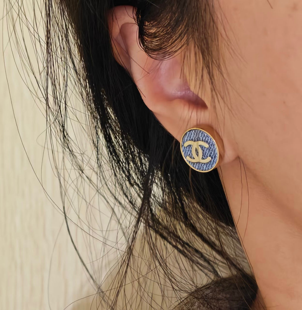 Chanel logo stud earrings worn on ear, featuring blue enamel and gold-tone