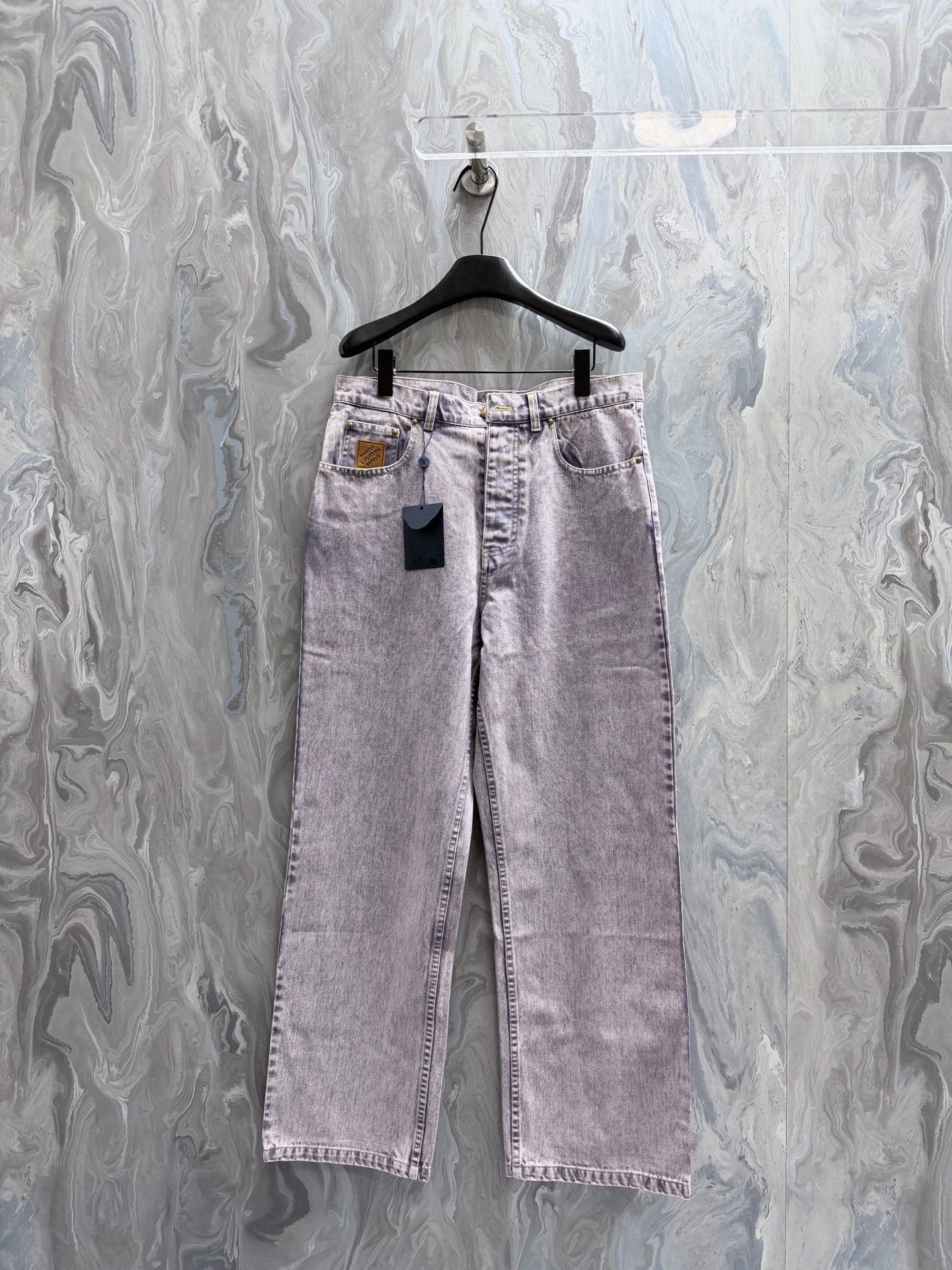 Denim pants in dark purple with front buttons and frayed hem, hanging on a hanger