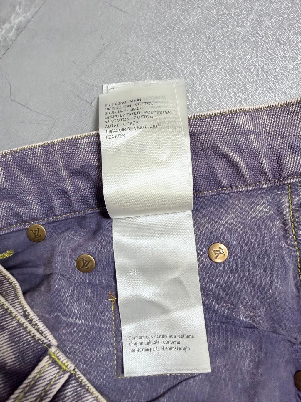 Denim pants waistband care label listing cotton and leather, with gold buttons