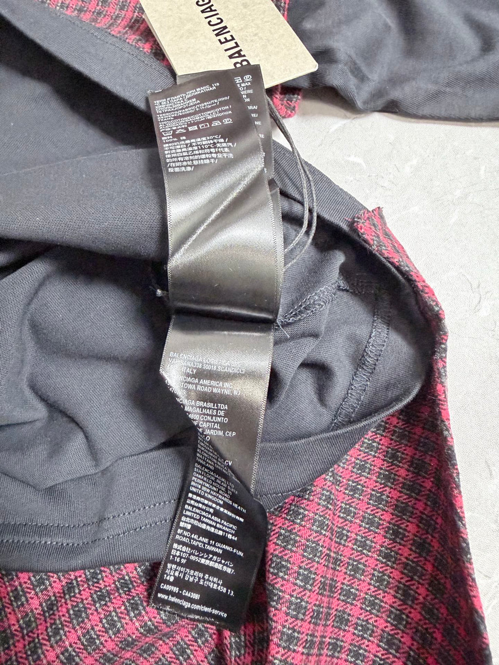 Long-sleeve jacket close-up: dark gray hood and burgundy check panel, care label and tag