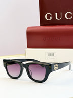 Gucci sunglasses with black acetate frames and purple-tinted lenses, gold logo on temple