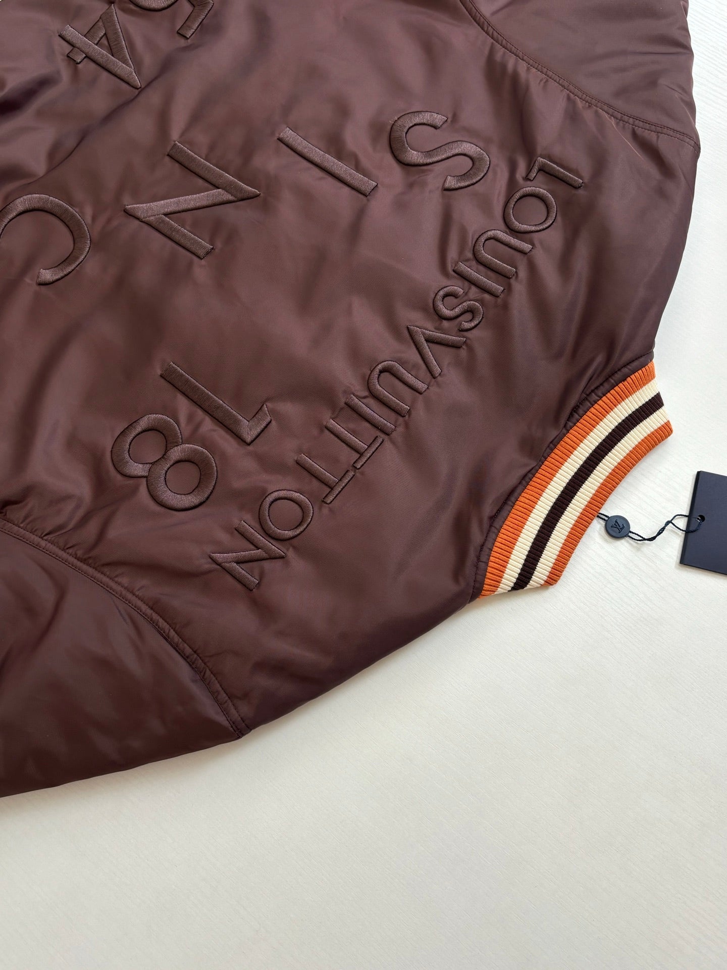 Dark brown long jacket with embroidered LV-style logo and striped orange-white-black trim