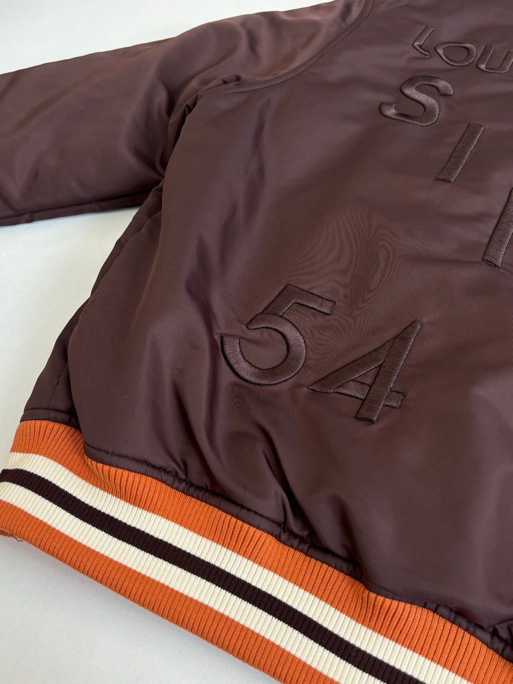 Dark brown long jacket with ribbed collar and striped orange-white-black sleeve trim