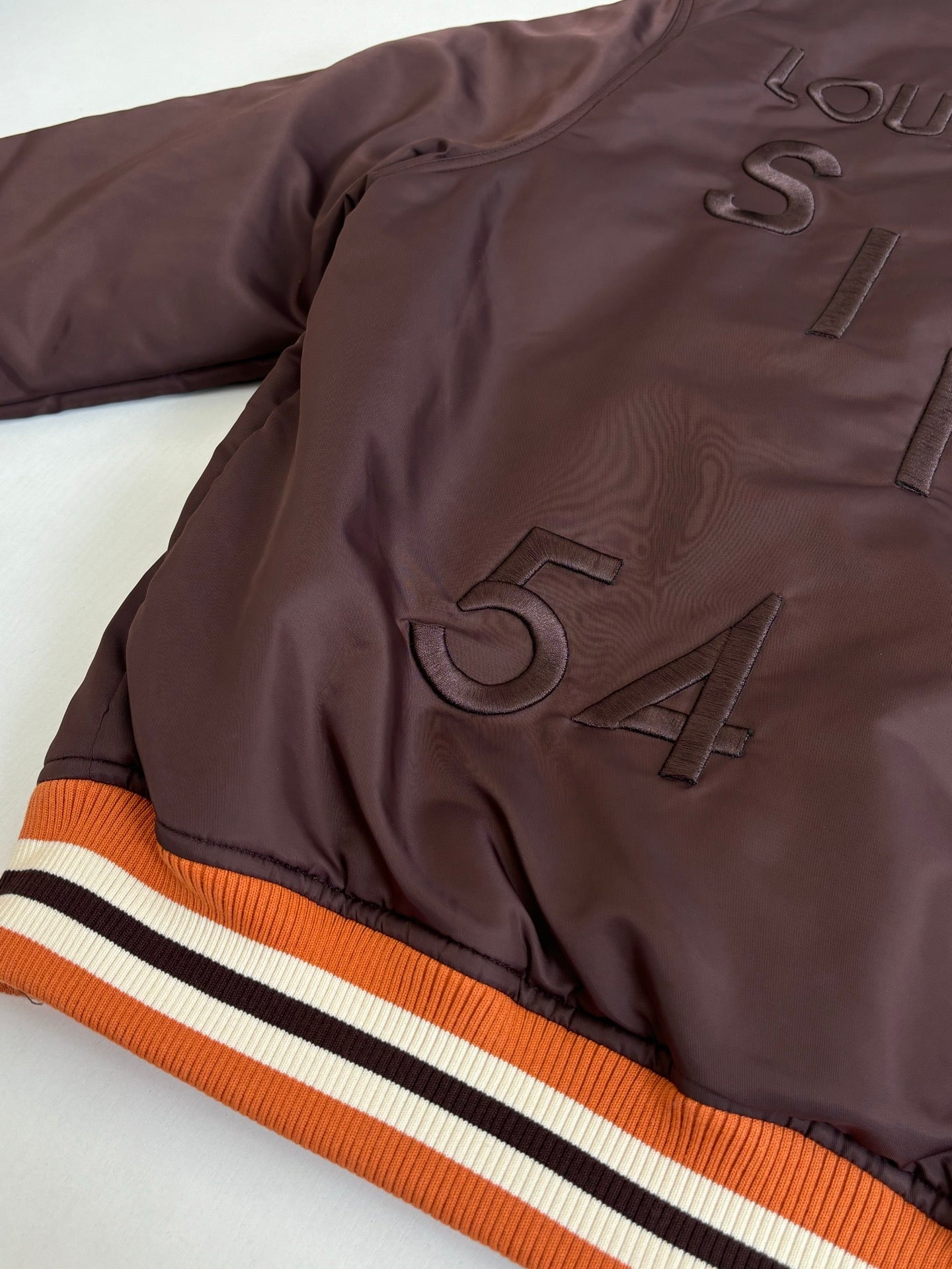 Dark brown long jacket with ribbed collar and striped orange-white-black sleeve trim