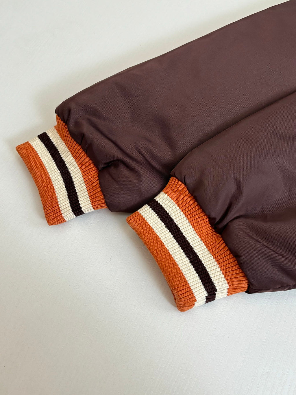 Dark brown long jacket with ribbed orange-white-black cuffs on folded sleeves