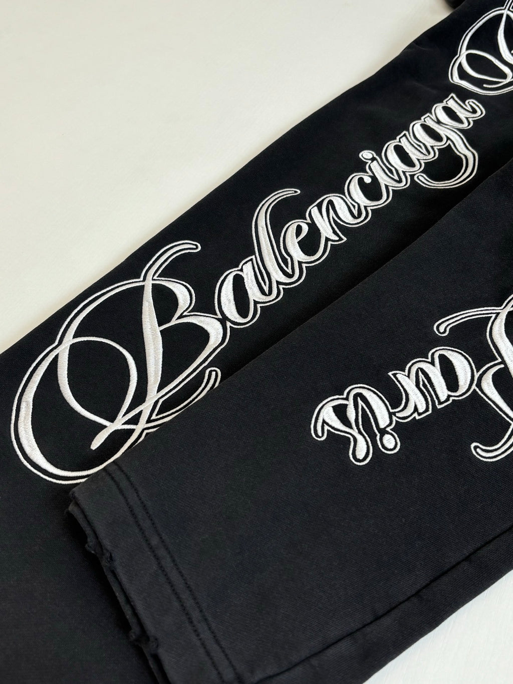 Black Balenciaga track pants with large white script logo along leg seam