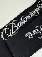 Black Balenciaga track pants with large white script logo along leg seam