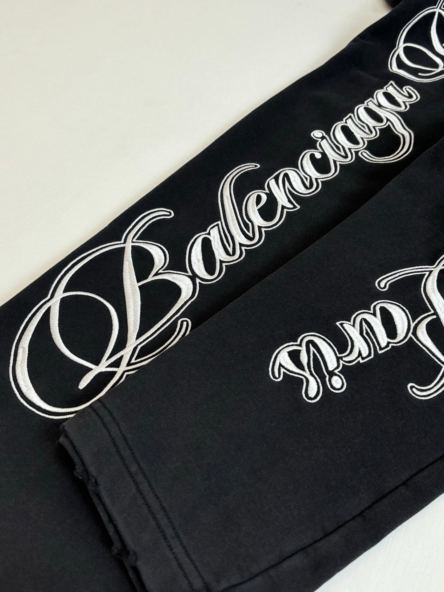 Black Balenciaga track pants with large white script logo along leg seam