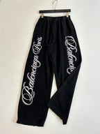 Black Balenciaga track pants with large side script logos, hanging on hanger