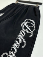 Black Balenciaga track pants with large white script logo on one leg