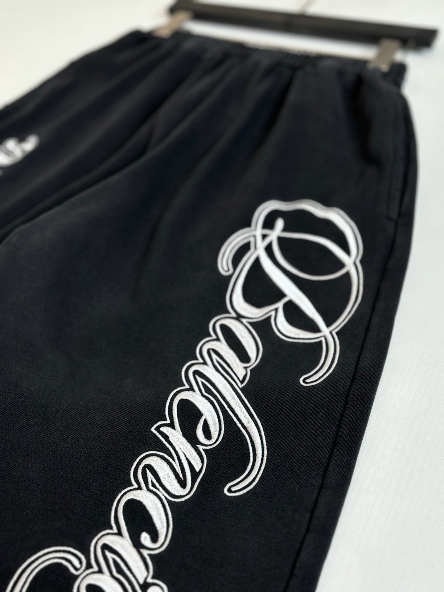 Black Balenciaga track pants with large white script logo on one leg
