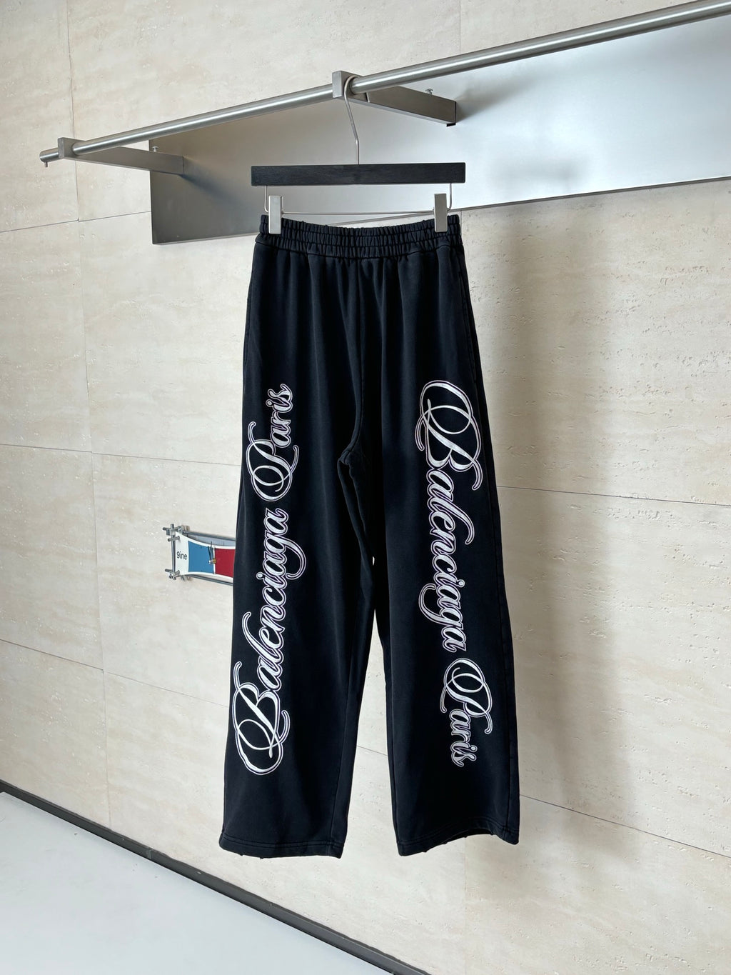 Black Balenciaga track pants with elastic waistband and wide leg, hanging on rack