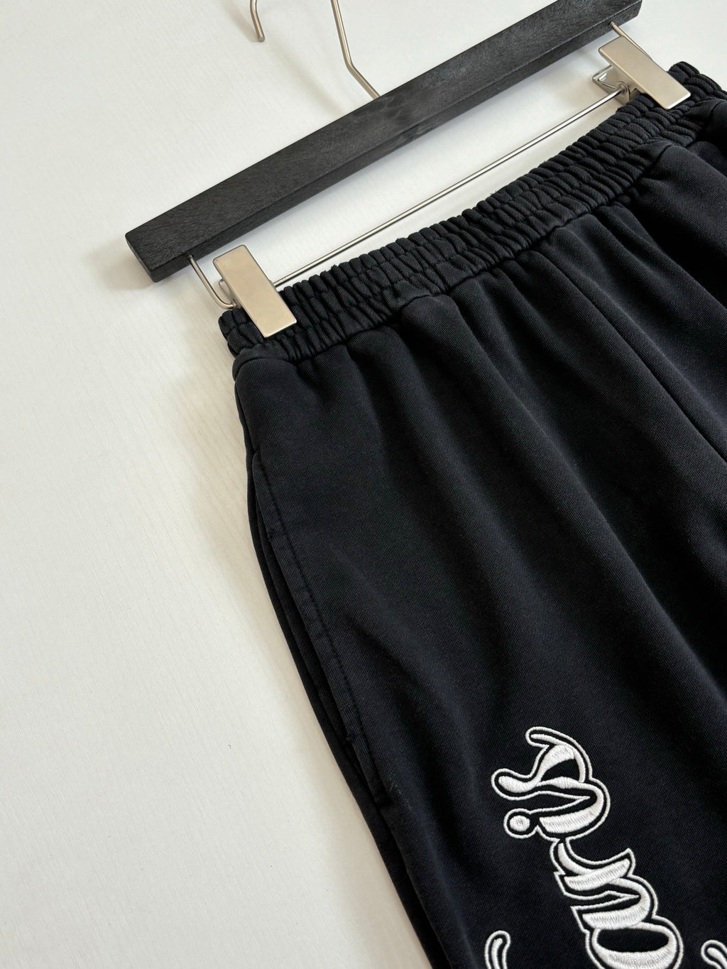 Black track pants with elastic waistband and small bird-style logo embroidery