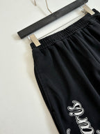 Black track pants with elastic waistband and small bird-style logo embroidery