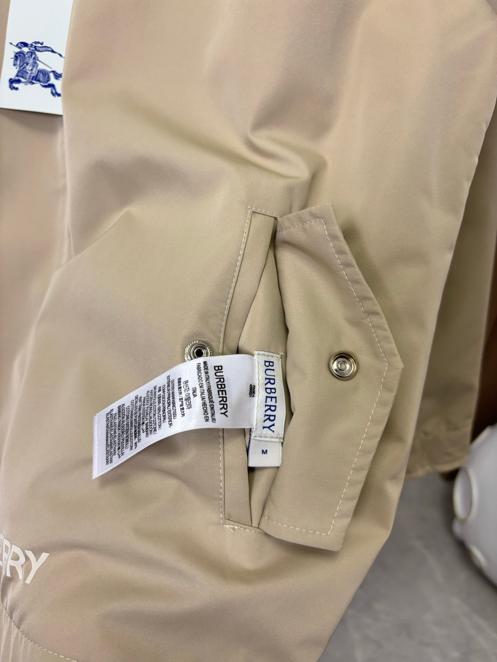 Beige jacket pocket detail with snap flap and attached brand tags