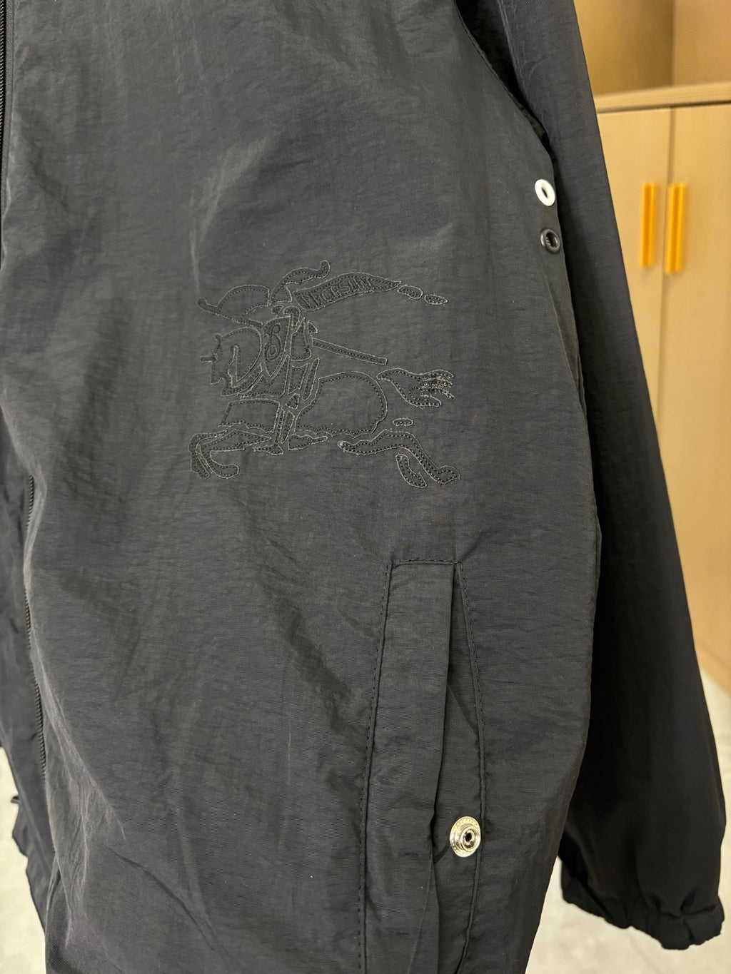 Dark jacket close-up with embroidered crest on chest and snap cuff button