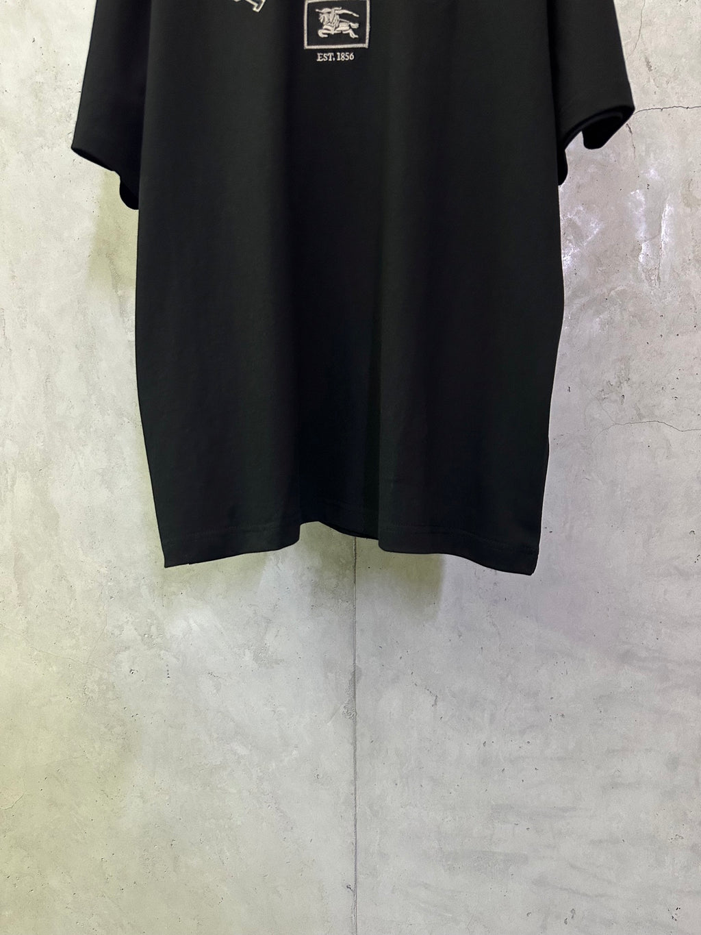 Black crewneck short-sleeve T-shirt, lower front with partial logo