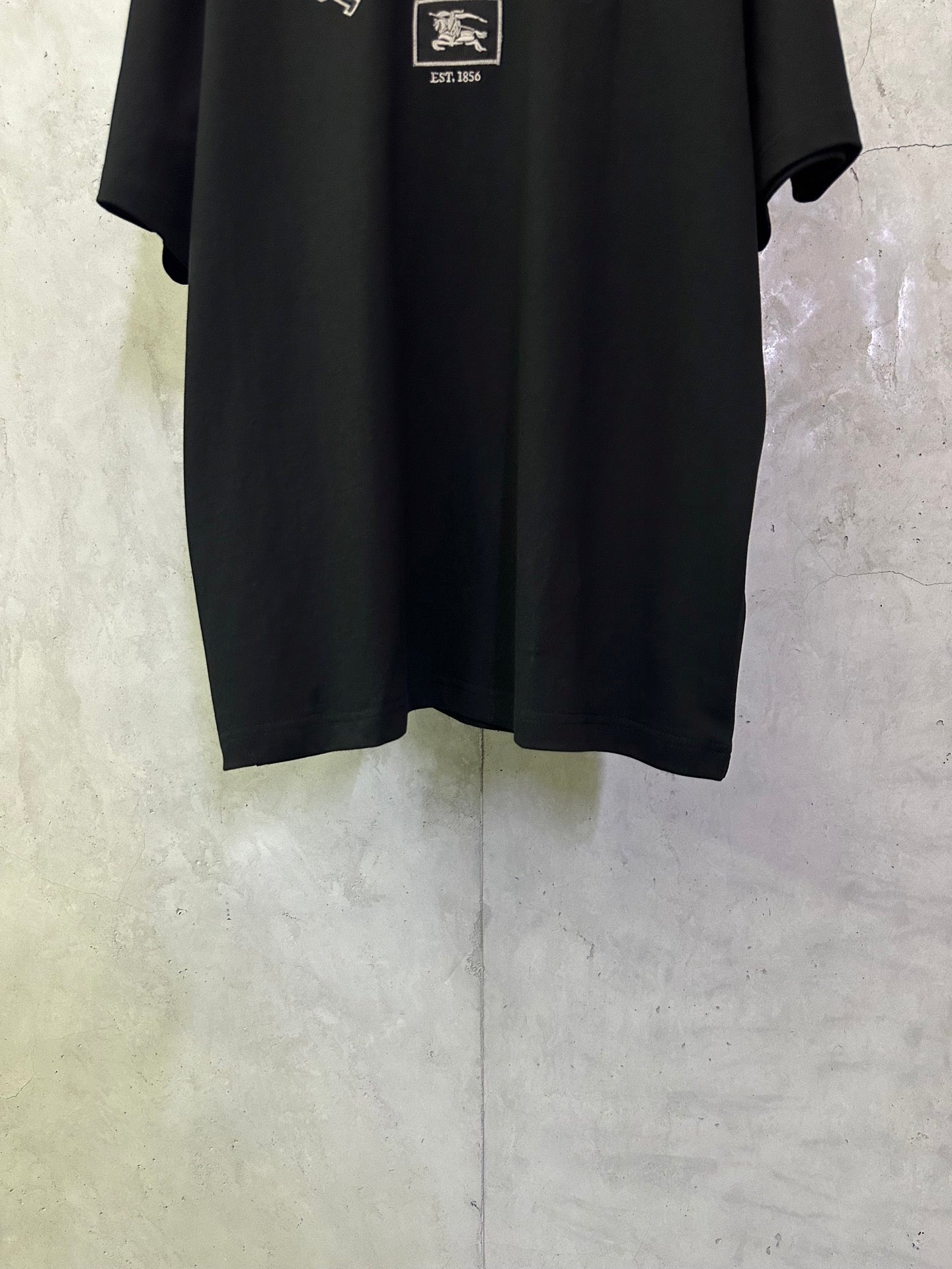 Black crewneck short-sleeve T-shirt, lower front with partial logo